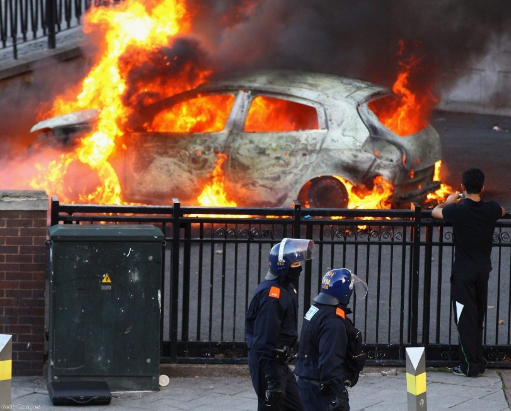Police walk by a burning car during the height of the rioting. The disorder forced a re-think on gang policy.