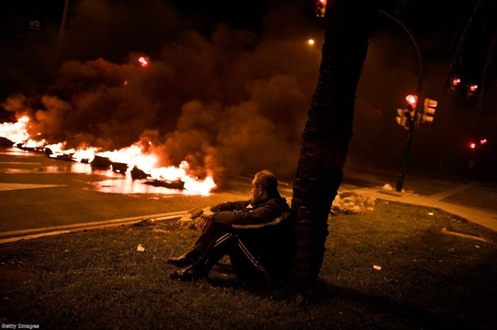 A demonstrator sits next to a barricade of burning tires at the main entrance of Mercabarna, the biggest wholesale market in Madrid, last night.