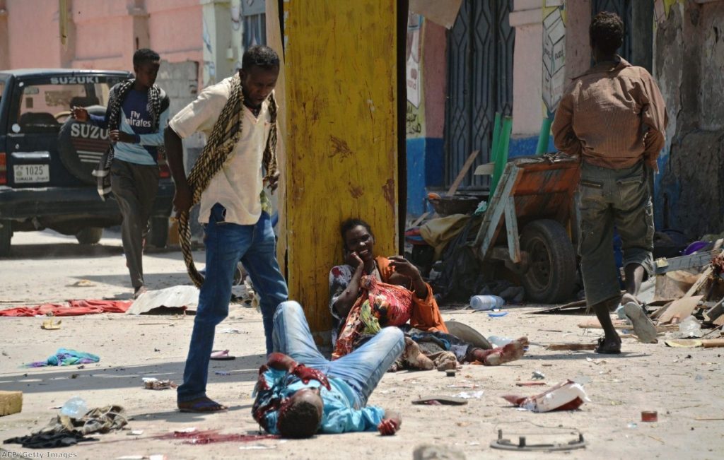 A Somali man looks down at a blast victim as a wounded Somali mother holds her two children, one wounded and one dead, following a bomb attack in Mogadishu last month
