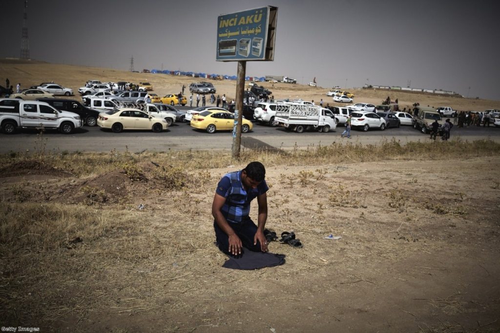 An Iraqi refugee fleeing from the city of Mosul prays at a checkpoint as he to enter Kurdistan