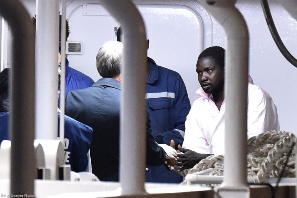 Italian minister Graziano Delrio shakes hands with a migrant standing on the deck of a boat carrying 27 survivors of the migrant shipwreck