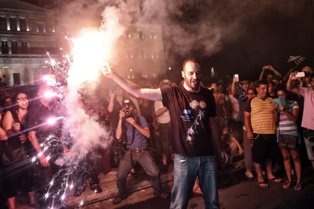 Greeks celebrate in front of the their parliament as the results from last night's vote start to come in