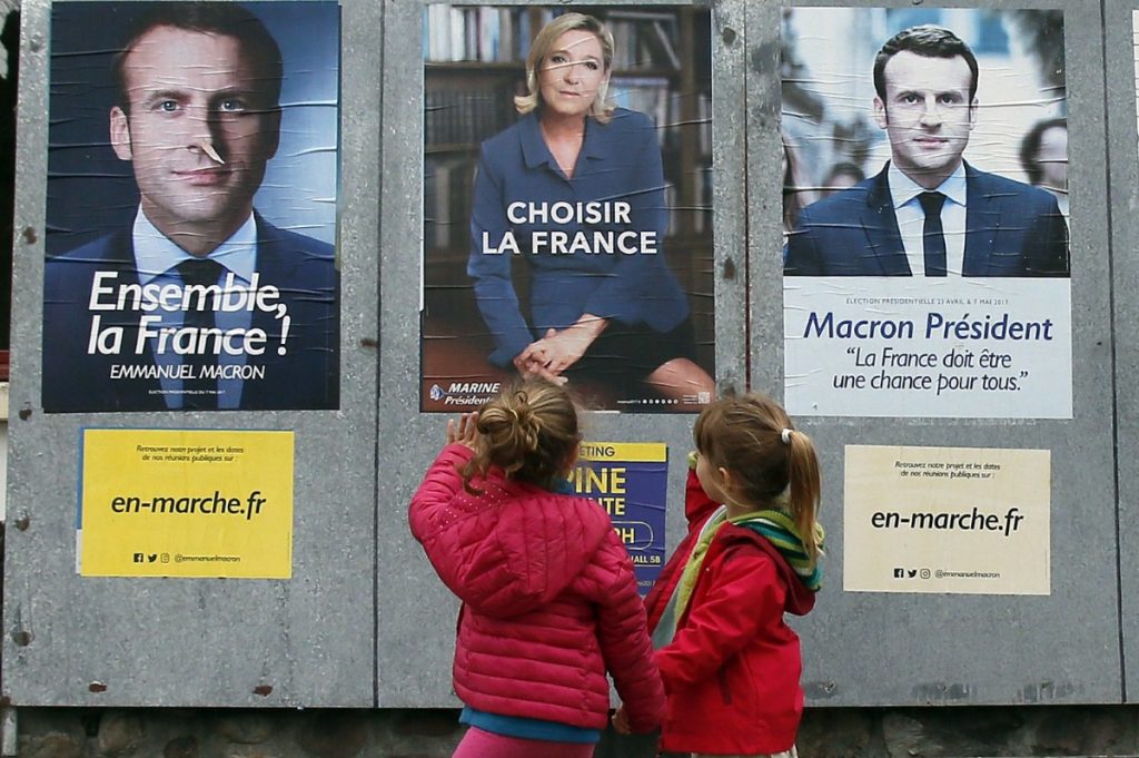 Children walk past election campaign posters for French centrist presidential candidate Emmanuel Macron and far-right candidate Marine Le Pen, in Osses, southwestern France.