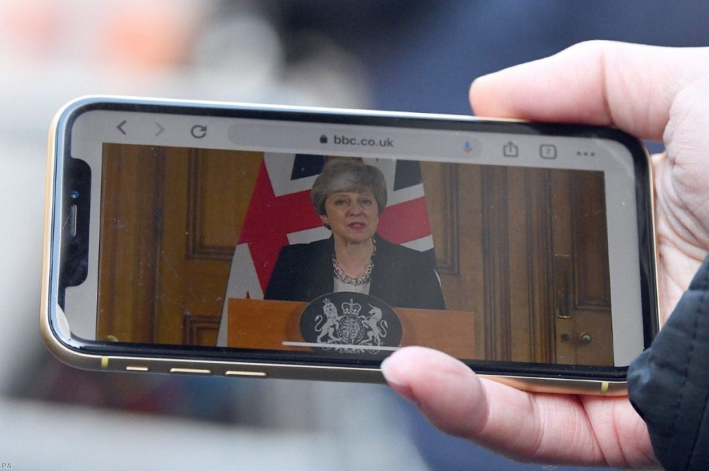 A journalist watches the prime minister's statement on a mobile phone this afternoon