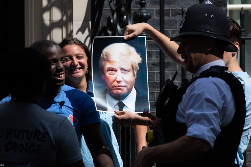 Campaigners for the youth group Ofoc hold up a poster melding Johnson and Trump's face as they hand in a petition to Downing Street.