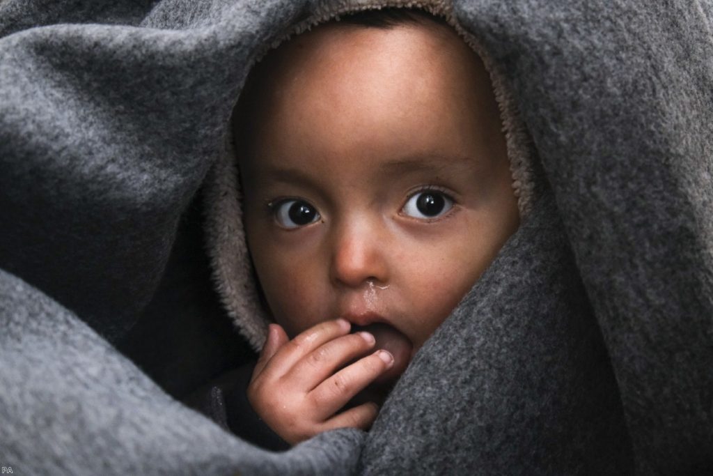 A migrant baby is wrapped in a blanket on the Greek island of Lesbos, after crossing on a dinghy from Turkey yesterday.